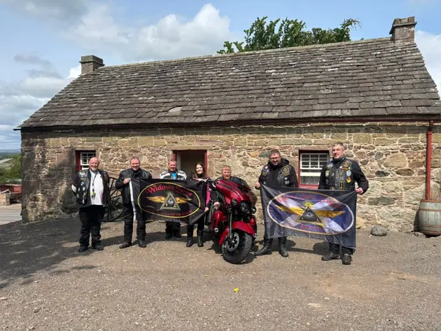 Motorcyclists with banners and bikes outside the single-storey stone Davidson Legacy Cottage