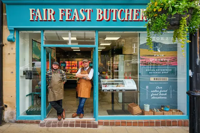 Two people in aprons and caps standing in the doorway of the Fair Feast butcher's shop