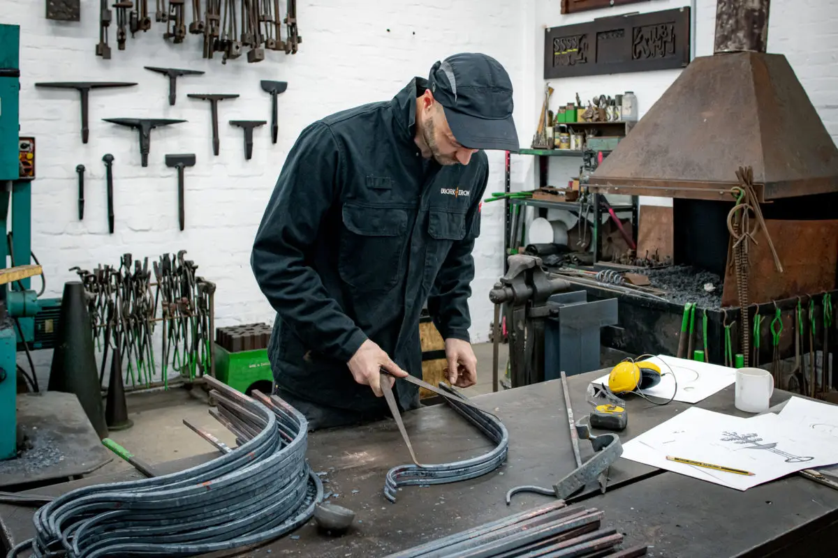 Jack, the blacksmith behind Work of Iron, shaping curved metal bars at a workbench in his forge